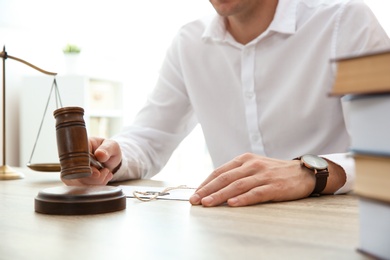 Photo of Judge with gavel at table in courtroom, closeup. Law and justice concept