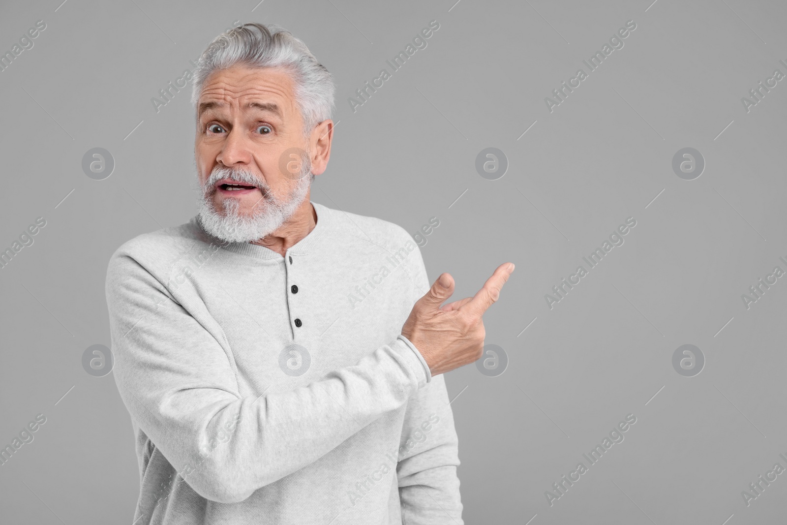 Photo of Surprised senior man pointing at something on grey background, space for text