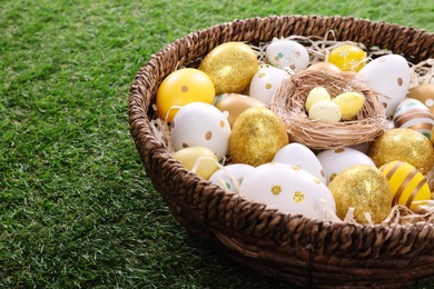 Photo of Many different Easter eggs in wicker basket on green grass, closeup