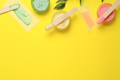 Flat lay composition with different types of wax and spatulas on yellow background. Space for text