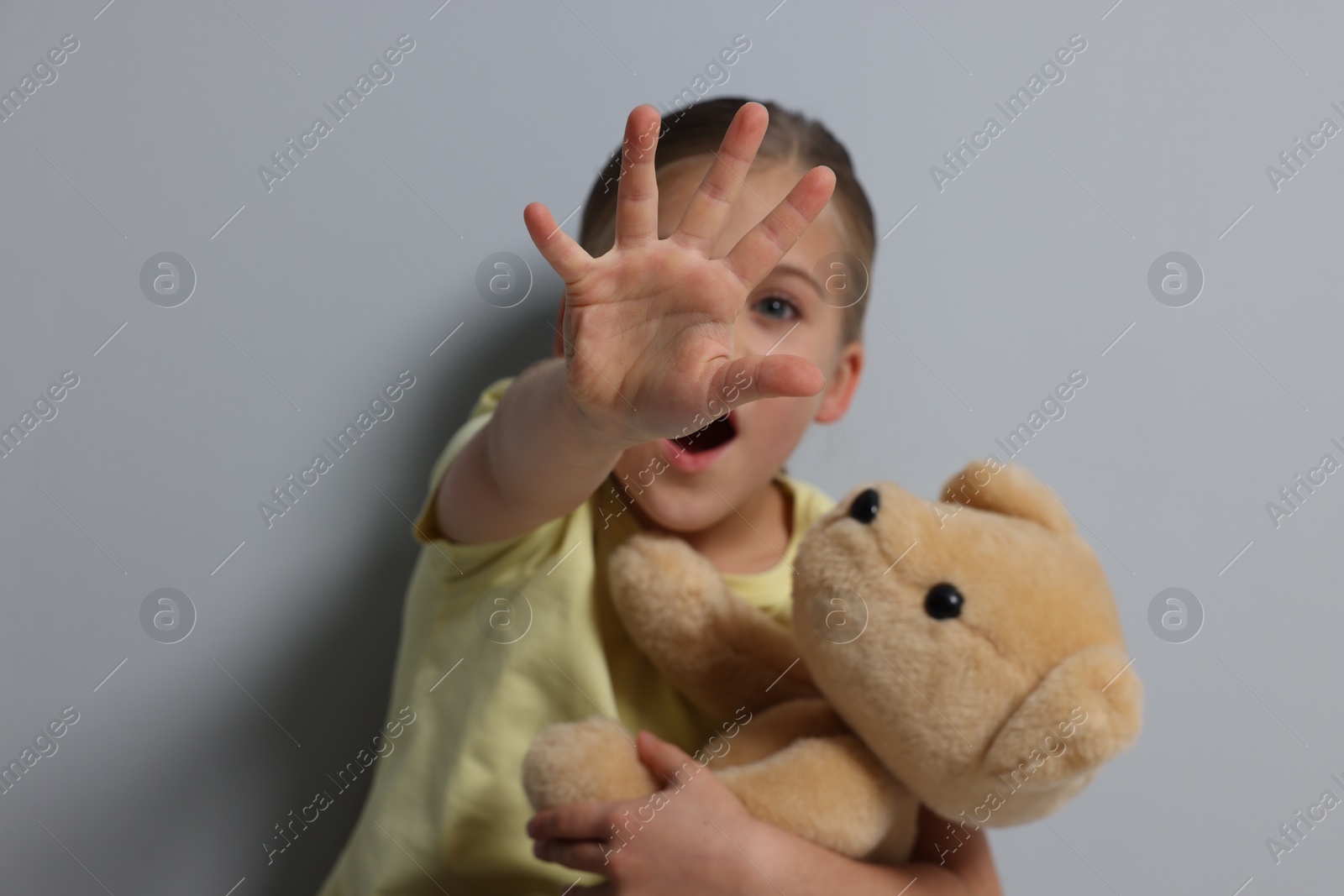 Photo of Child abuse. Girl with toy making stop gesture near grey wall, selective focus