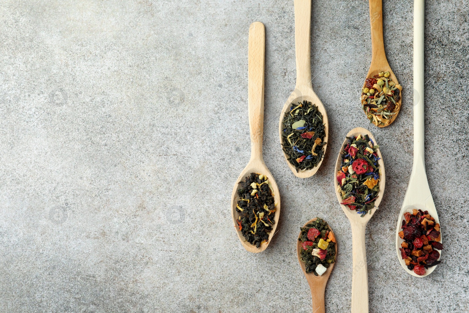 Photo of Different kinds of dry herbal tea in wooden spoons on light grey table, flat lay. Space for text