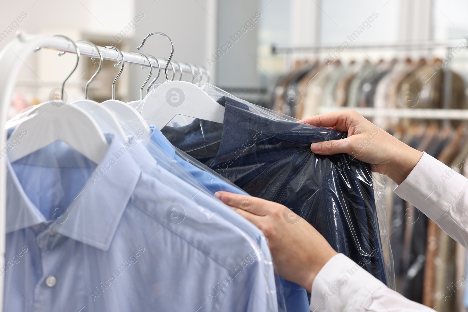 Photo of Dry-cleaning service. Woman taking shirt in plastic bag from rack indoors, closeup