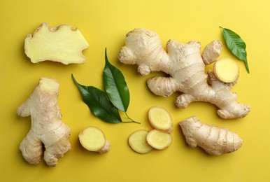 Photo of Fresh ginger with green leaves on pale light yellow background, flat lay