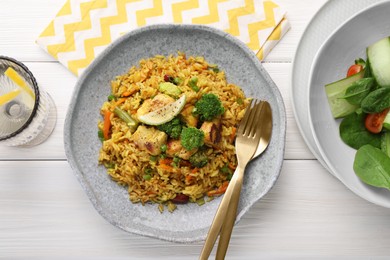 Tasty rice with meat and vegetables in plate served on white wooden table, flat lay