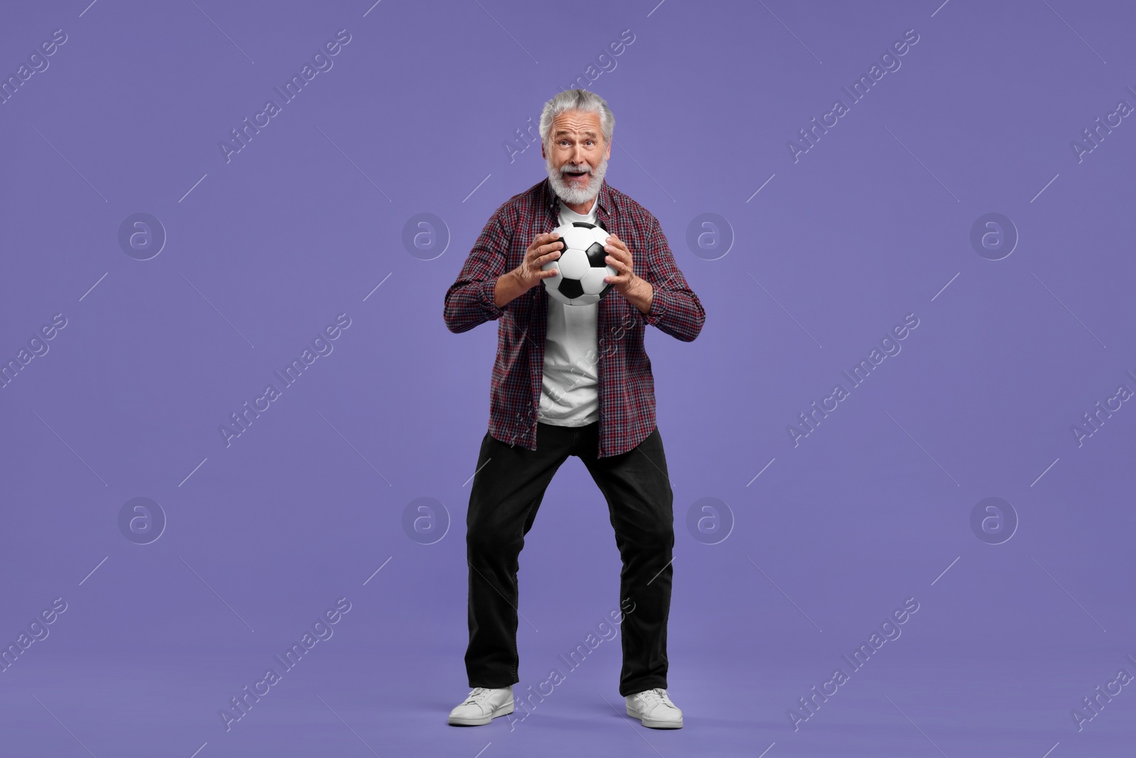 Photo of Emotional senior sports fan with soccer ball on purple background