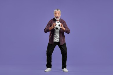 Photo of Emotional senior sports fan with soccer ball on purple background