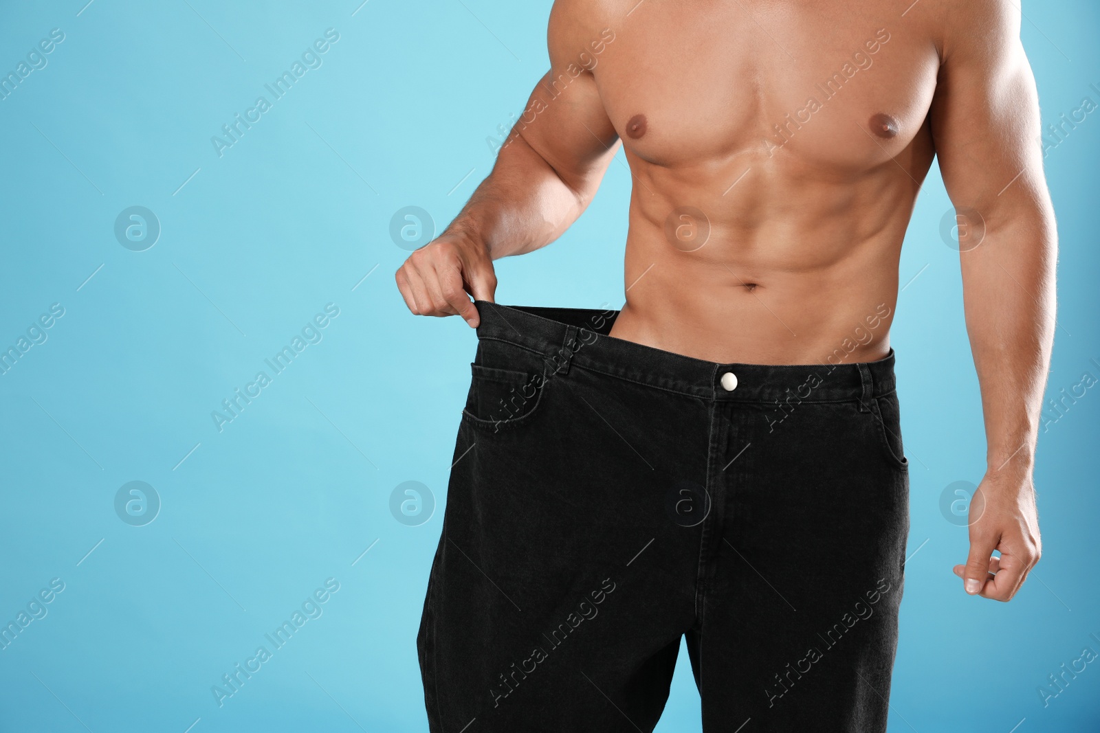 Photo of Young man with slim body in old big size jeans on light blue background, closeup view. Space for text