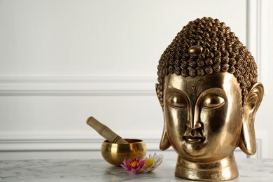 Photo of Buddha statue near lotus flowers and singing bowl on white marble table. Space for text