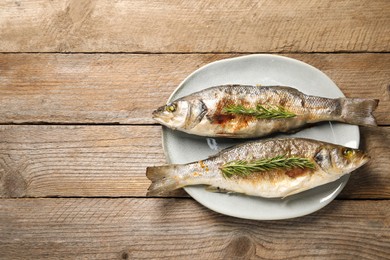 Photo of Delicious baked fish and rosemary on wooden table, top view. Space for text