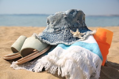 Denim hat, slippers, towel, starfish and sunscreen on sandy beach., closeup