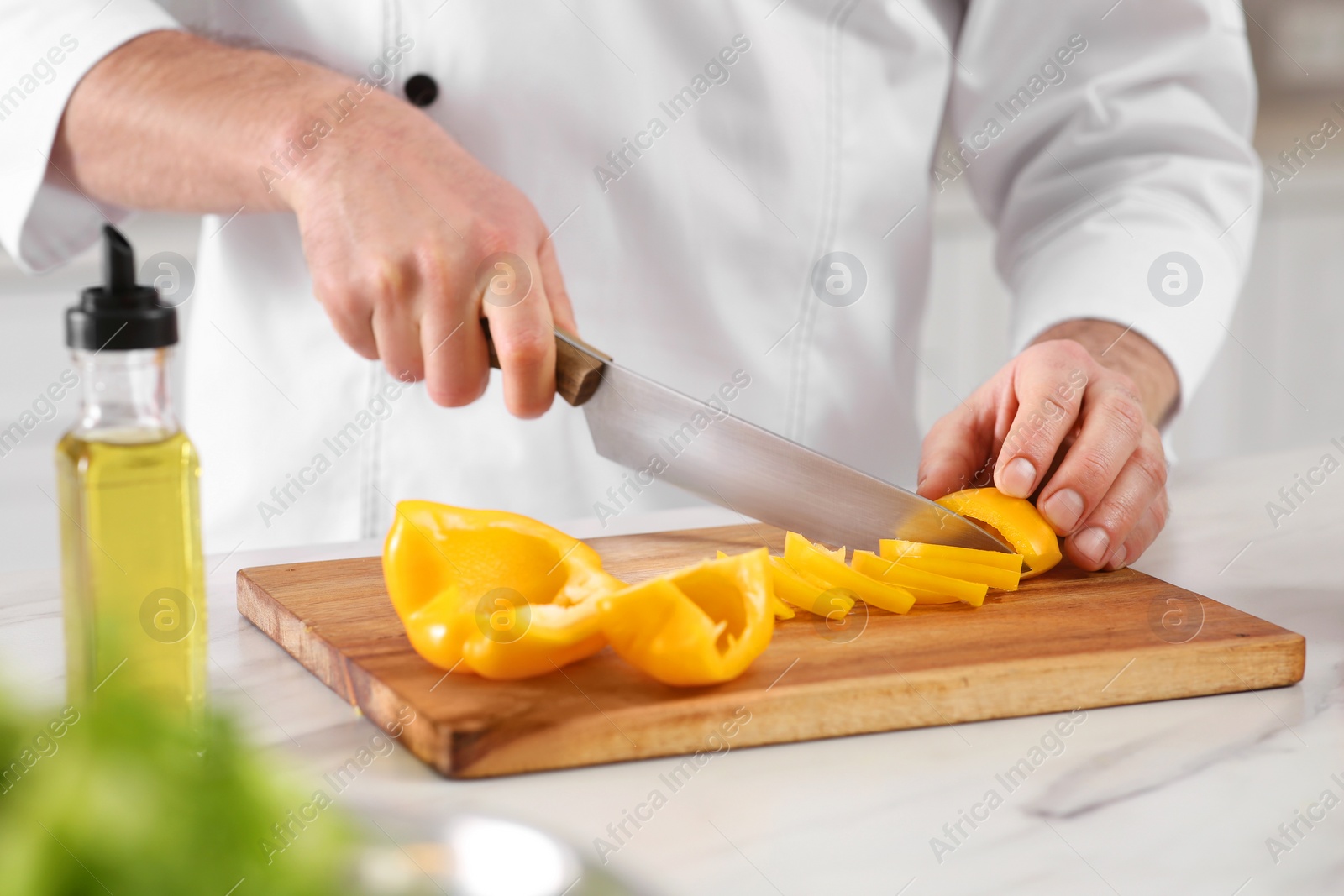 Photo of Chef cutting bell pepper at marble table, closeup