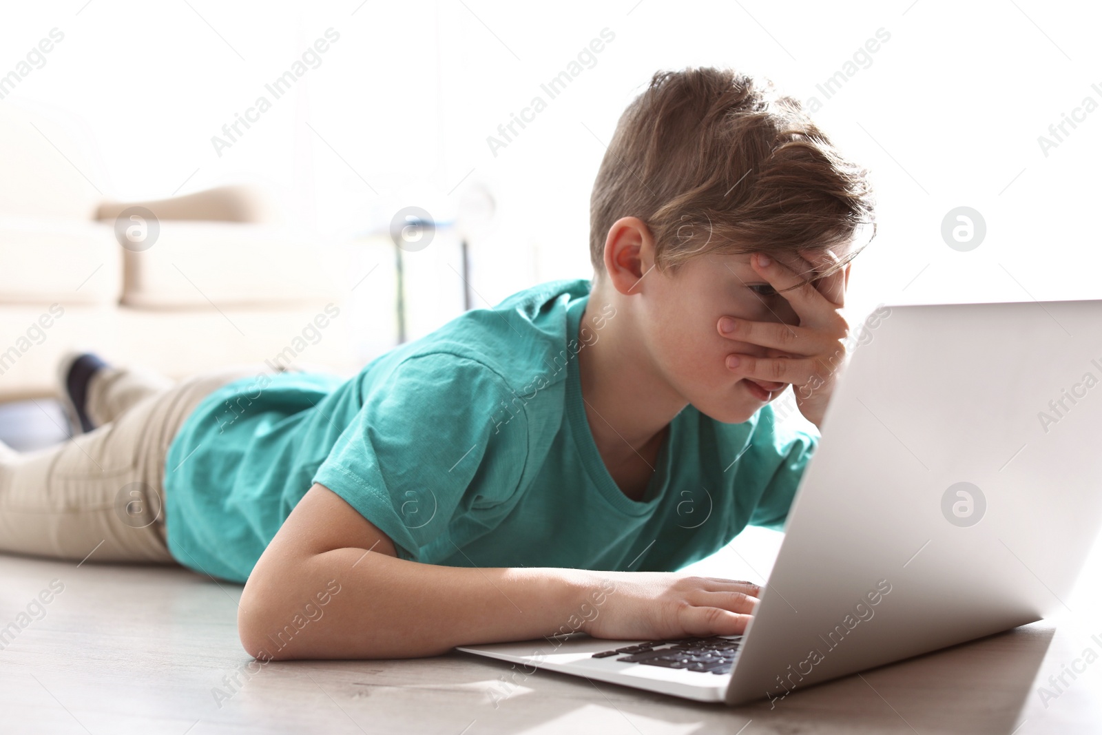 Photo of Scared and curious little child with laptop on floor indoors. Danger of internet