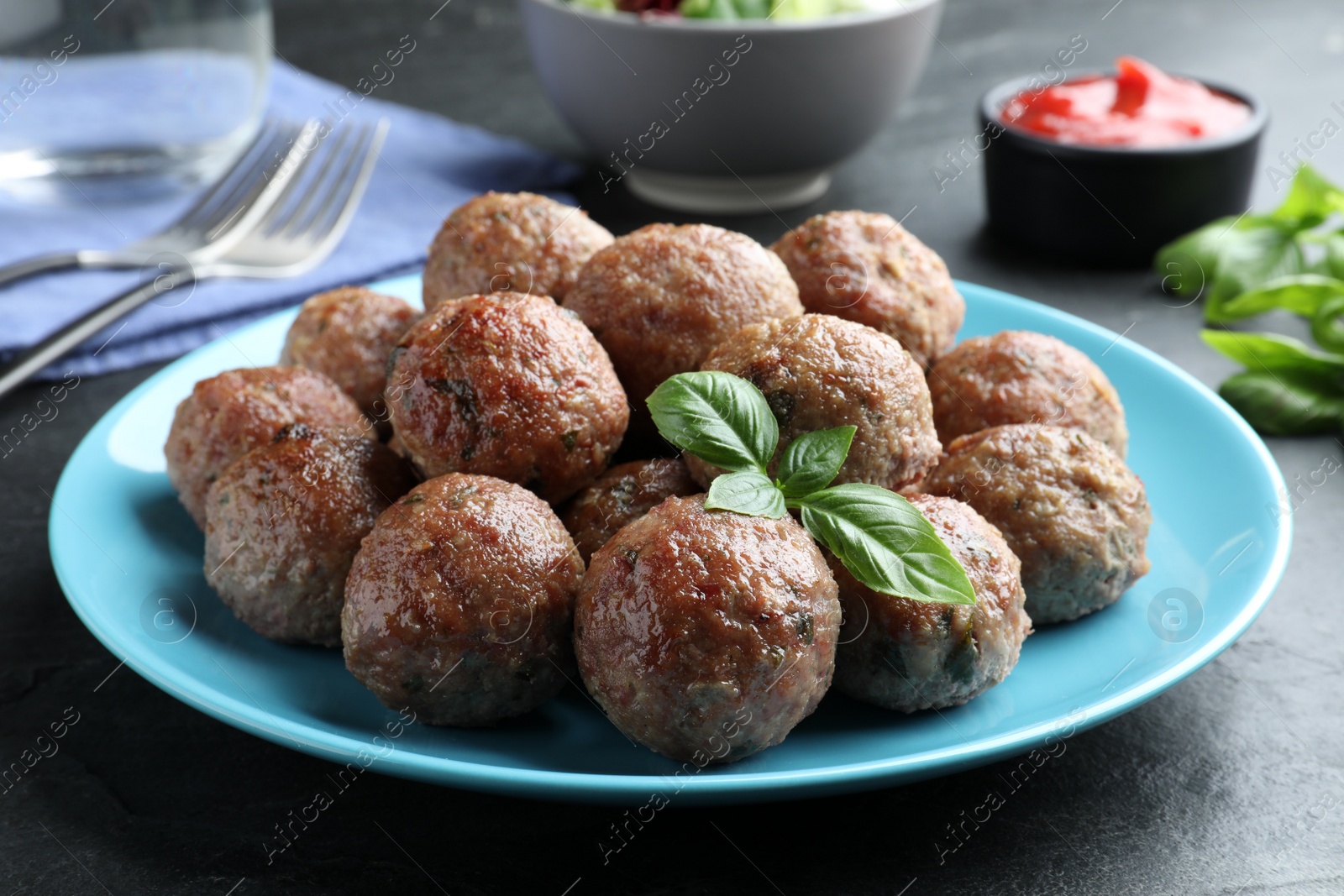 Photo of Tasty cooked meatballs with basil on black table, closeup