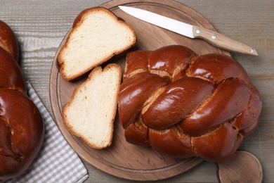 Photo of Cut homemade braided bread and knife on wooden table, flat lay. Challah for Shabbat