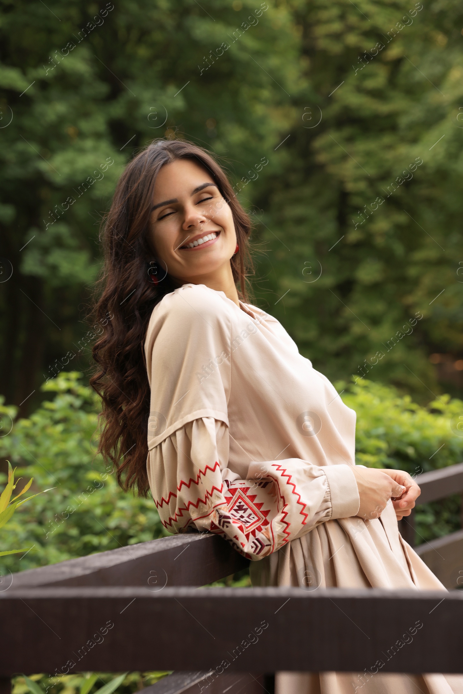 Photo of Beautiful woman wearing embroidered dress near wooden railing in countryside. Ukrainian national clothes