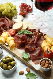 Photo of Charcuterie board. Delicious bresaola and other snacks served on white marble table