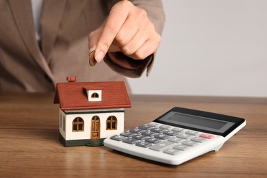 Photo of Mortgage concept. Woman putting coin into house model at wooden table, closeup with space for text