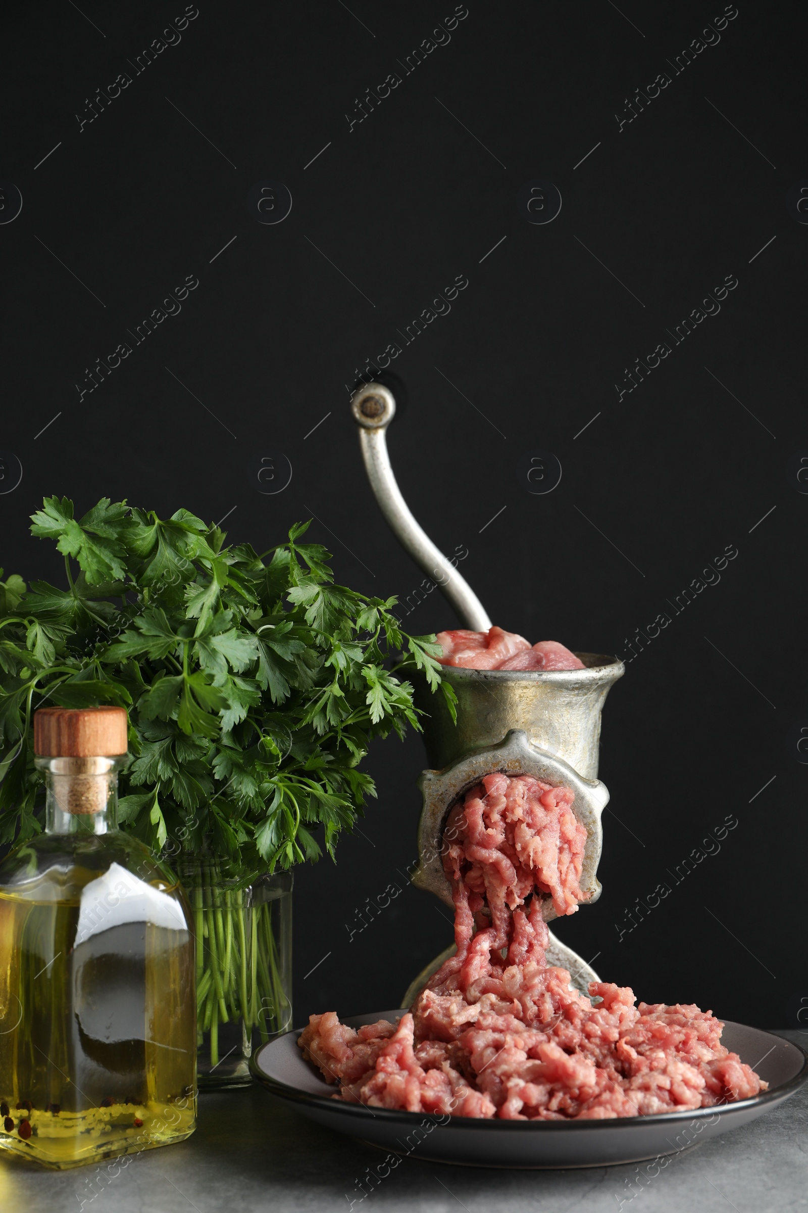 Photo of Manual meat grinder with beef mince, oil and parsley on grey table