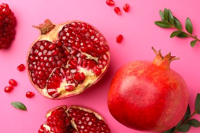 Photo of Fresh pomegranates and green leaves on pink background, flat lay