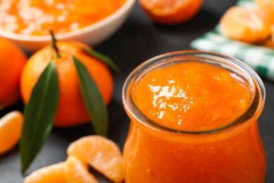 Photo of Tasty tangerine jam in glass jar on dark table, closeup. Space for text