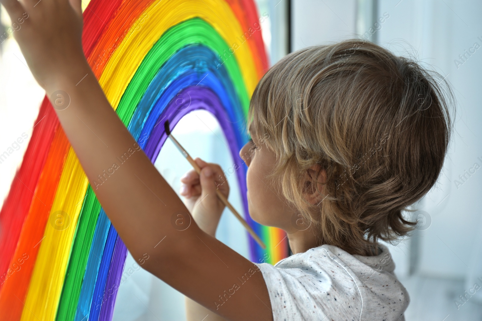 Photo of Little boy drawing rainbow on window. Stay at home concept