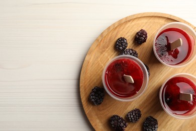 Photo of Tasty berry ice pops in plastic cups and space for text on white wooden table, top view. Fruit popsicle