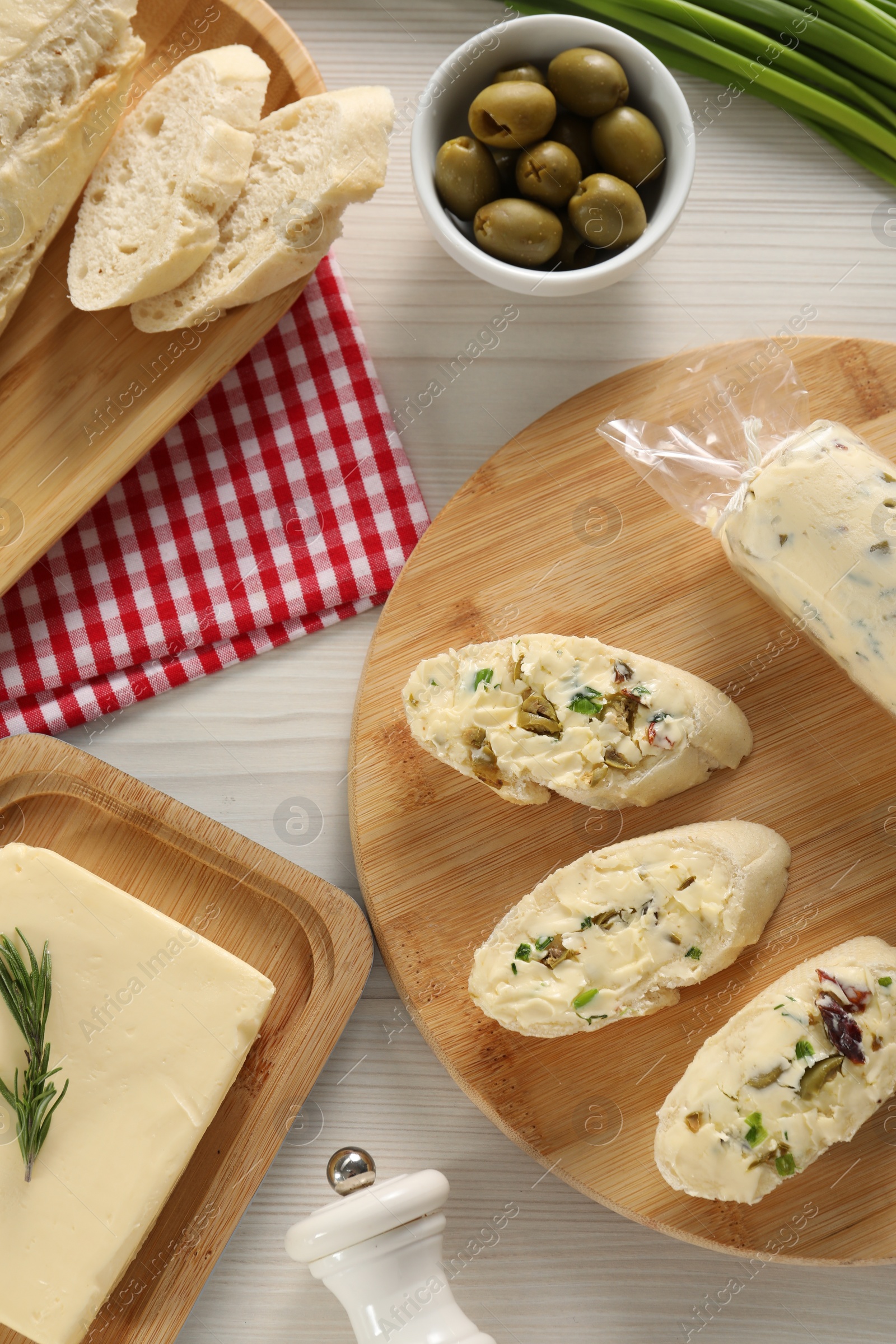 Photo of Tasty butter, olives, green onion and bread on wooden table, flat lay