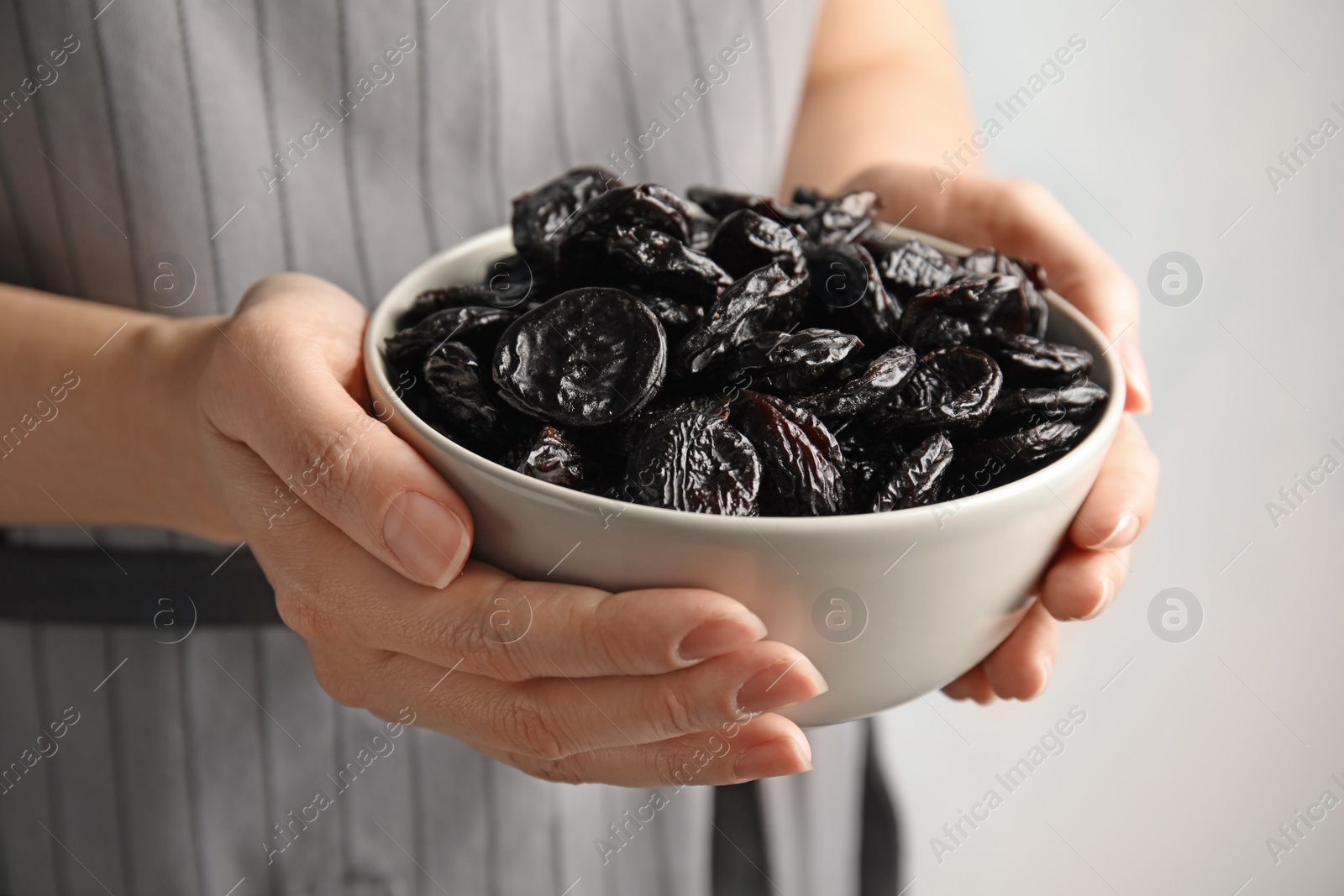 Photo of Woman holding bowl of dried plums, closeup. Healthy fruit