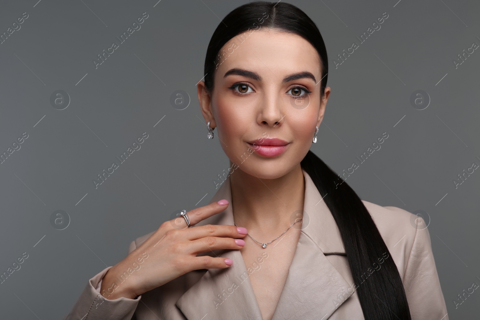 Photo of Beautiful young woman with elegant jewelry on dark grey background