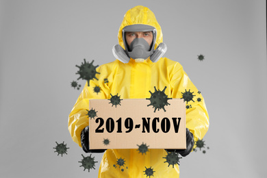 Man wearing chemical protective suit with cardboard box on light grey background. Coronavirus outbreak