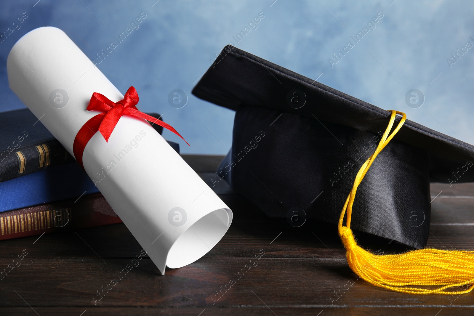 Photo of Graduation hat, books and student's diploma on black wooden table against light blue background