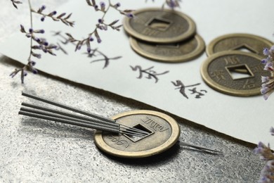 Photo of Acupuncture needles, Chinese coins, flowers and paper with characters on grey textured table, closeup