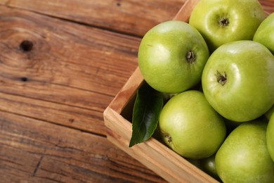 Photo of Fresh ripe green apples in crate on wooden table, closeup. Space for text