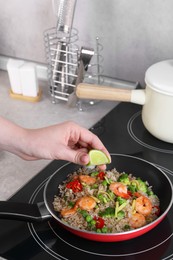 Photo of Woman squeezing lime into rice with shrimps and vegetables on induction stove, closeup