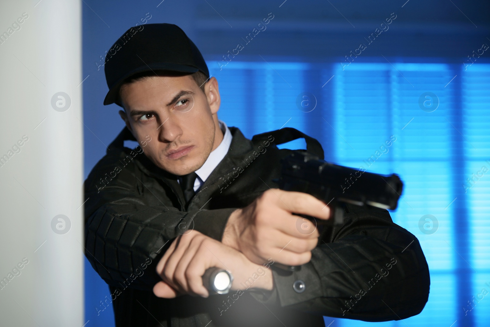 Photo of Professional security guard with flashlight and gun in dark room