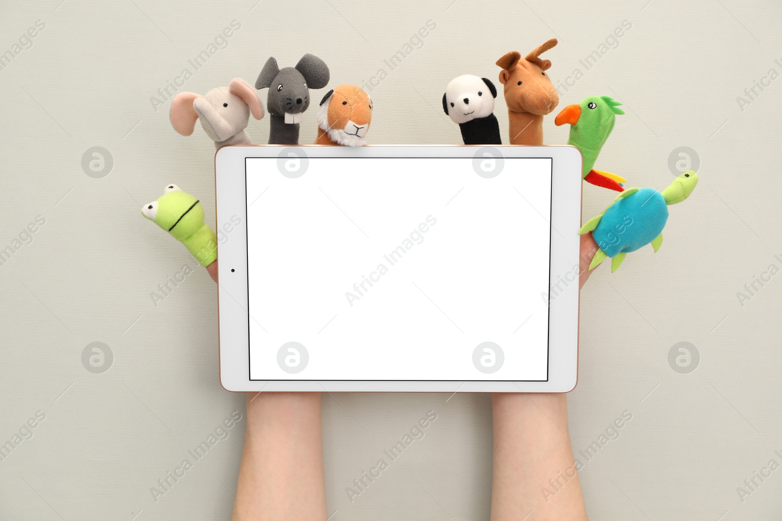 Photo of Person with animal puppets on fingers holding tablet against light background, closeup. Space for text