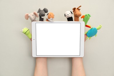 Person with animal puppets on fingers holding tablet against light background, closeup. Space for text