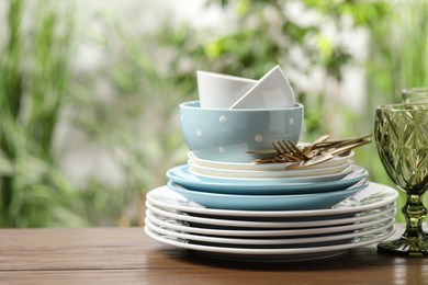 Photo of Beautiful ceramic dishware, glass and cutlery on wooden table outdoors, space for text