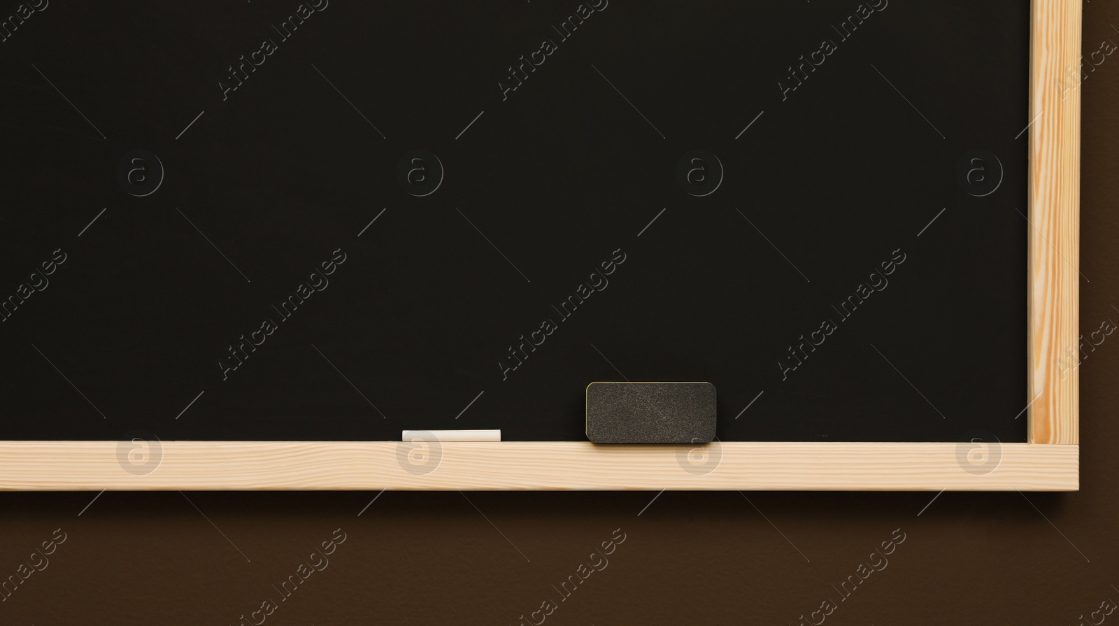 Photo of Clean blackboard with chalk and duster hanging on brown wall