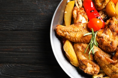 Wok with barbecued chicken wings and garnish on wooden background, top view. Space for text