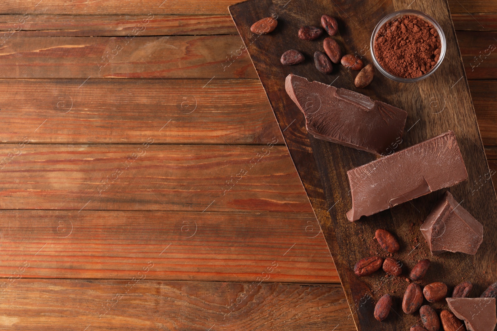 Photo of Pieces of tasty milk chocolate, cocoa beans and powder on wooden table, top view. Space for text