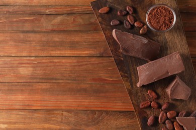 Photo of Pieces of tasty milk chocolate, cocoa beans and powder on wooden table, top view. Space for text