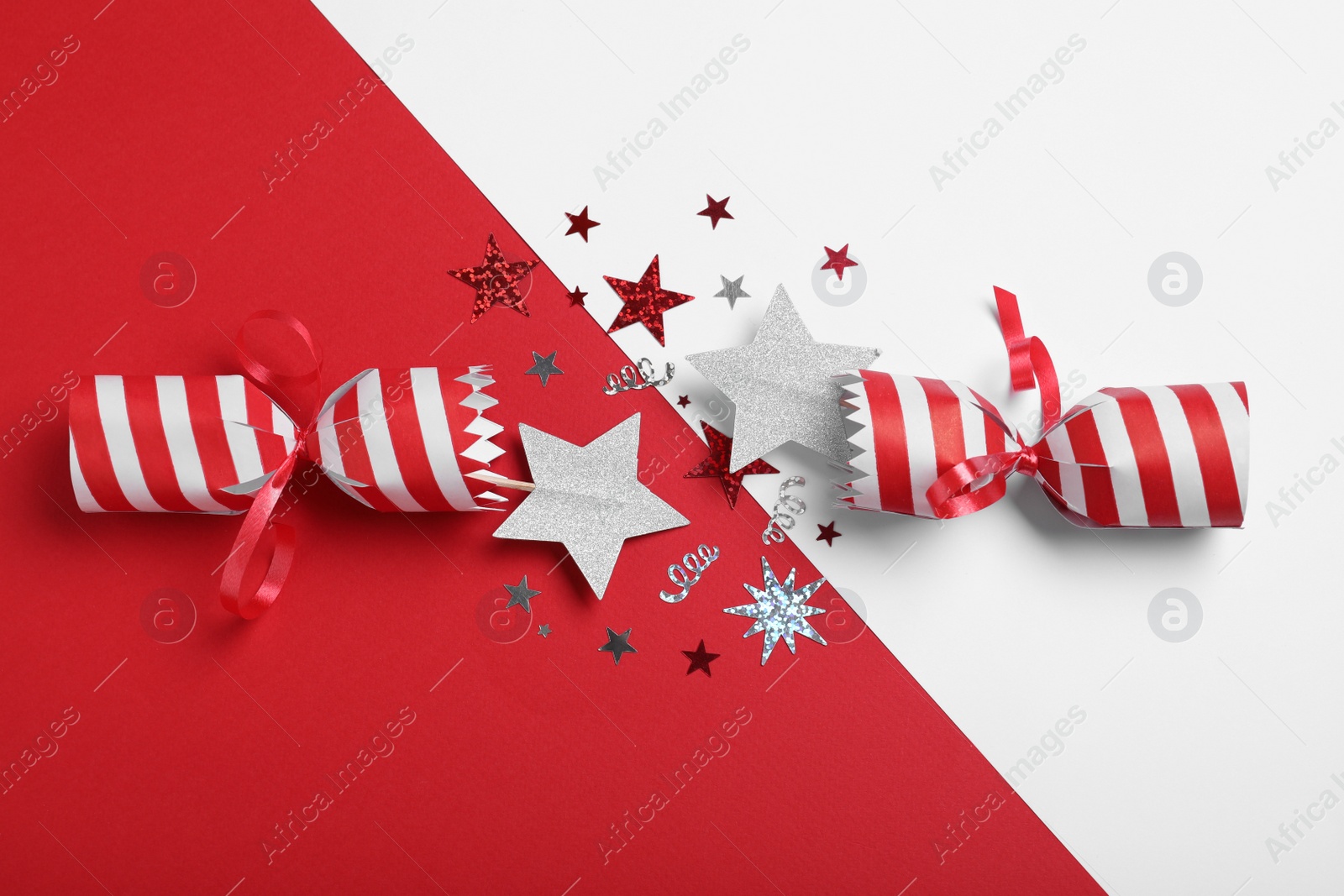 Photo of Open Christmas cracker with shiny confetti on color background, top view