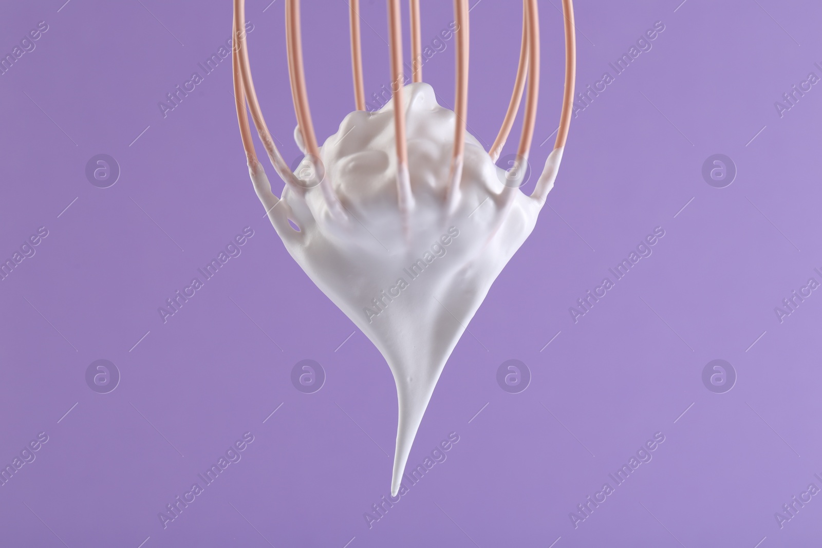 Photo of Whisk with whipped cream on violet background, closeup