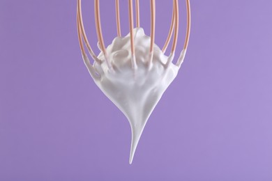 Photo of Whisk with whipped cream on violet background, closeup