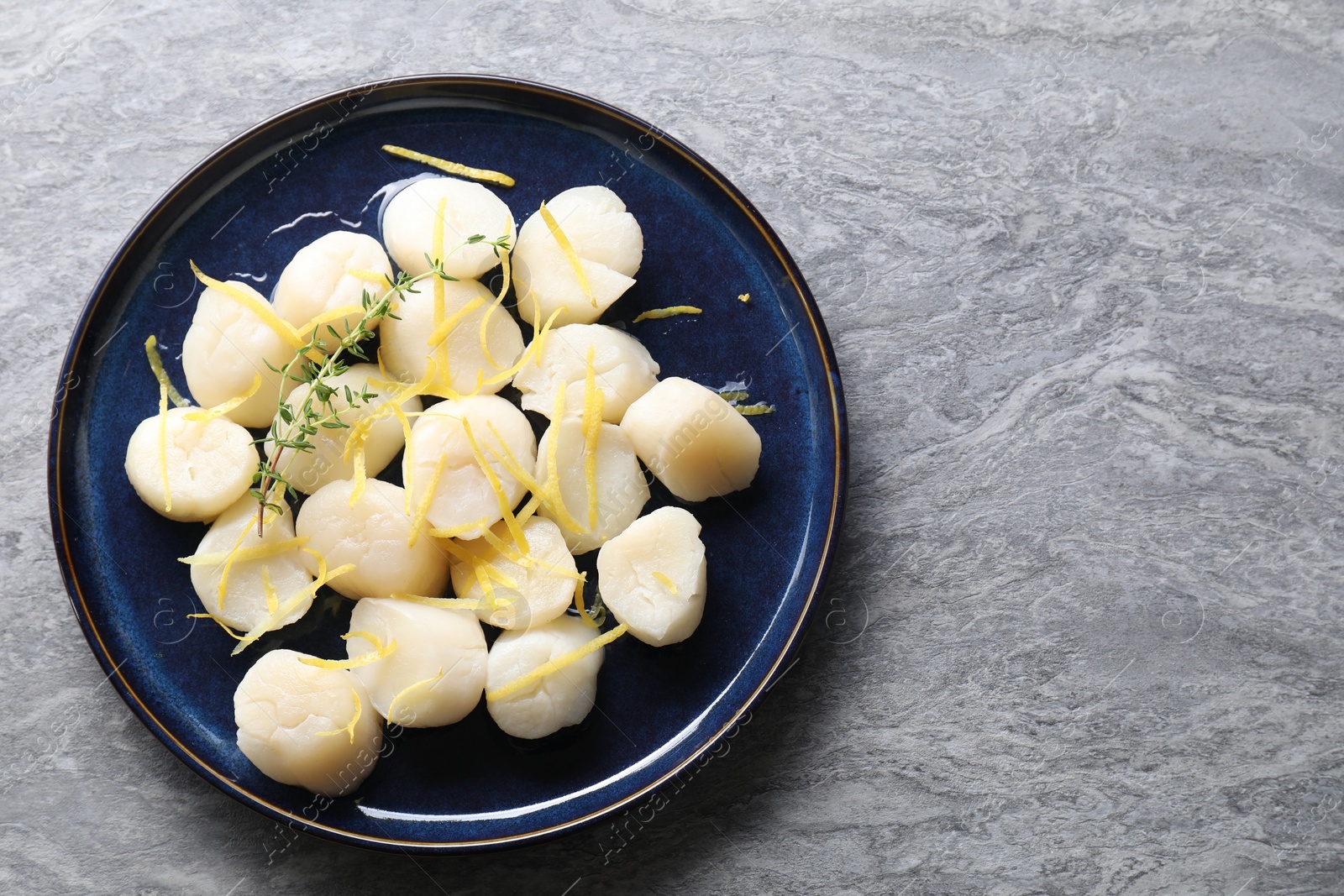 Photo of Raw scallops with thyme and lemon zest on grey marble table, top view. Space for text