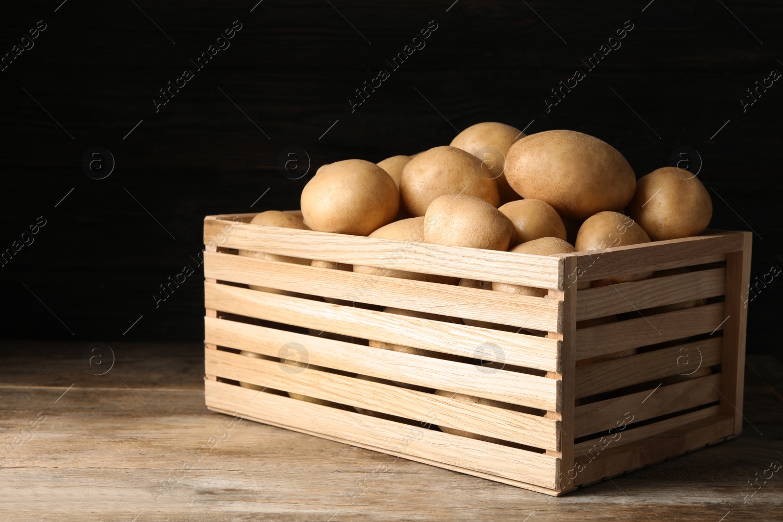 Photo of Raw fresh organic potatoes on wooden table against dark background