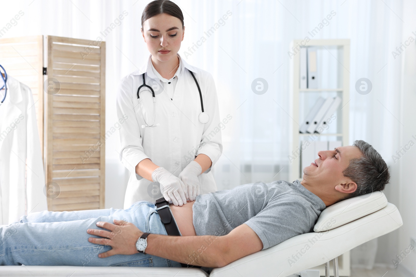 Photo of Gastroenterologist examining patient with stomach pain on couch in clinic