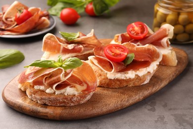 Photo of Board of tasty sandwiches with cured ham, basil, tomato and cream cheese on grey table, closeup